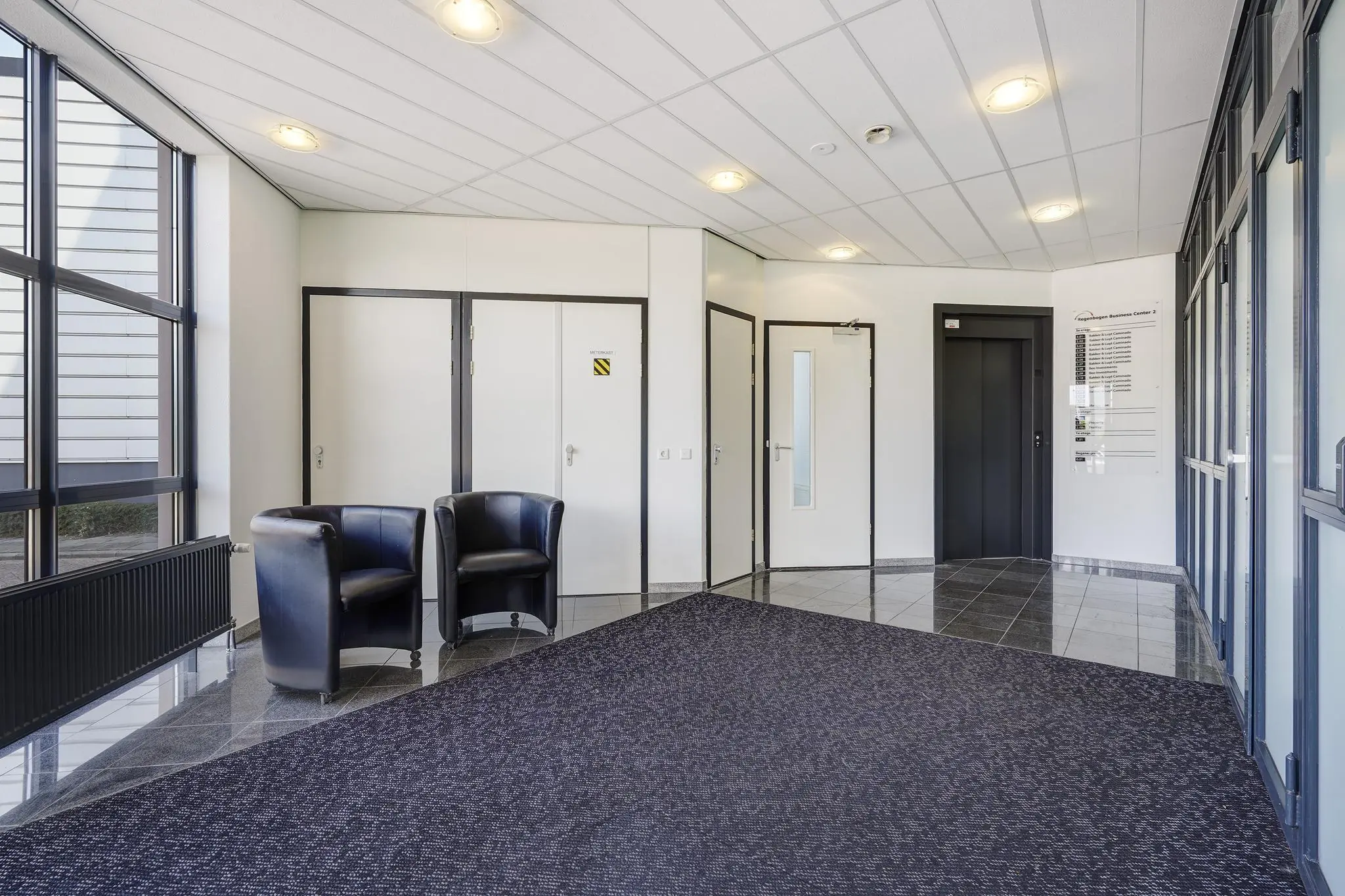 Moderne ontvangsthal van een kantoorpand aan de Laan van 's-Gravenmade met zwarte stoelen, lift en binnendeuren.